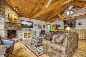 Ein gemütliches Wohnzimmer mit Kamin aus Stein, Holzbalken, einem Ledersofa und einem großen Gemälde.