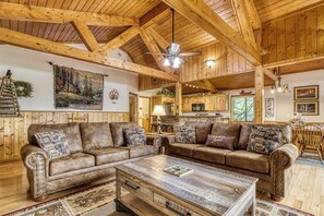 A rustic cabin interior with wooden beams, a large painting, a dining area, and a kitchen. - Cabin w/Mountain Views-Pool Table-Private Hot Tub (Gatlinburg)