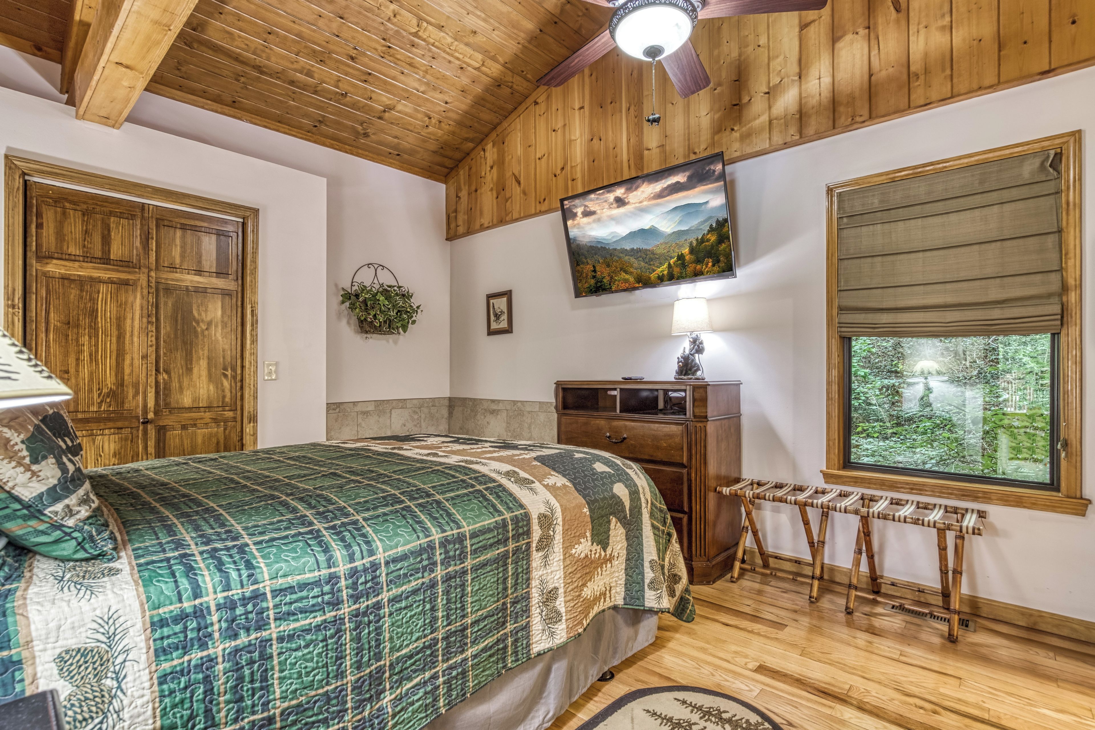 Un dormitorio con cama, techo de madera, televisor, ventana y escritorio.