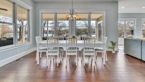 Un espace repas comprenant une grande table et des chaises, un lustre et de grandes fenêtres donnant sur l’extérieur.