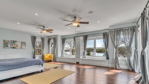 Une chambre spacieuse avec un grand lit, deux ventilateurs de plafond et une vue sur un lac, visible à travers de grandes fenêtres.