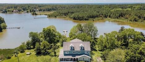 Una casa con un porche amplio, rodeada por un lago y un bosque denso.