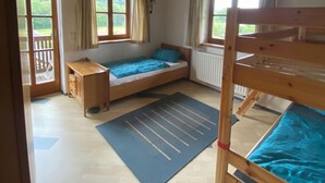Een knus kamertje met een stapelbed, een enkel bed, een bureau en een raam met gordijnen.
