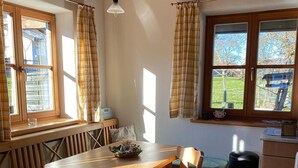 Een gezellig eetgedeelte met een houten tafel en bankjes, een raam met gordijnen, en uitzicht op de omgeving.