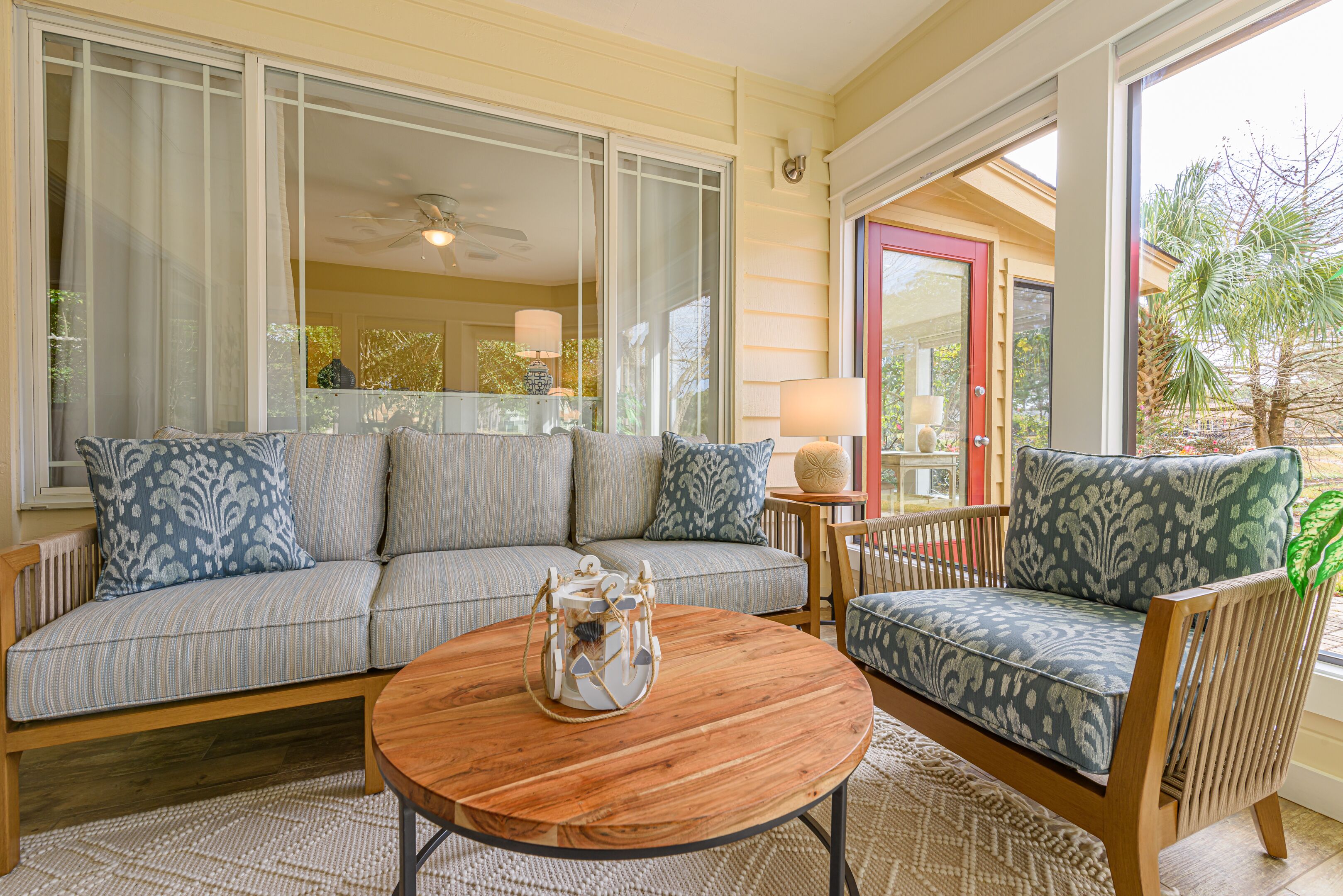 A cozy living room with a sofa, a chair, a round wooden coffee table, and a large window with curtains.