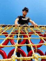 Una persona de pie sobre un puente colgante con cuerdas amarillas y obstáculos circulares rojos.