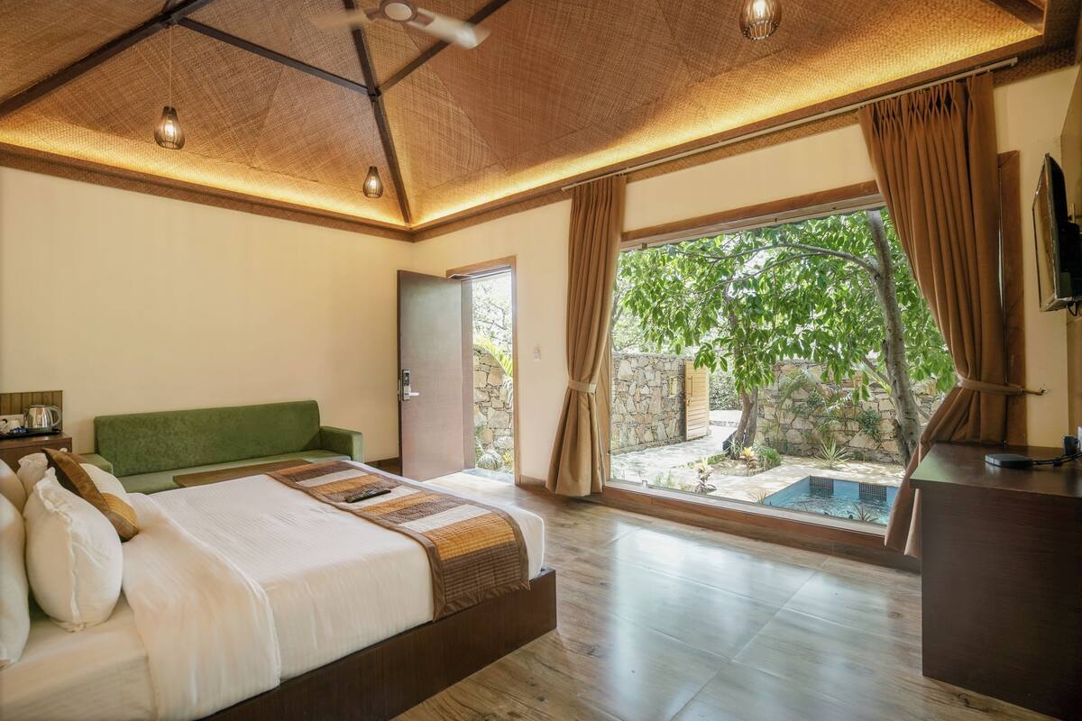 A bedroom with a large bed, a green headboard, a wooden desk, and a view of a swimming pool.