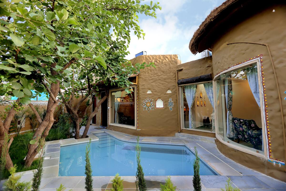 A pool area with a clear view of the pool, surrounded by a building with large windows and a thatched roof.