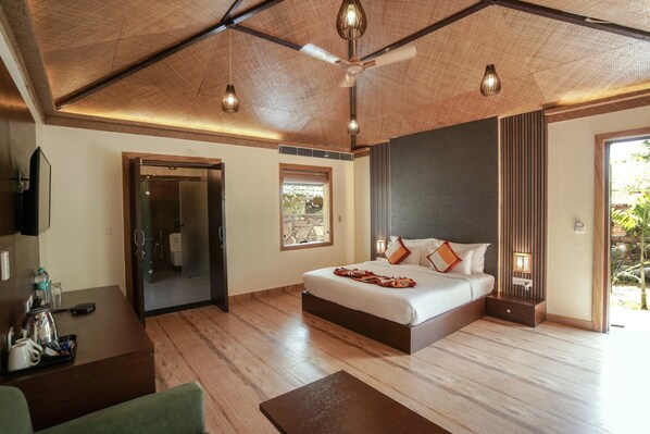 A hotel room with a bed, a desk, a chair, a ceiling fan, and a view of the outdoors.