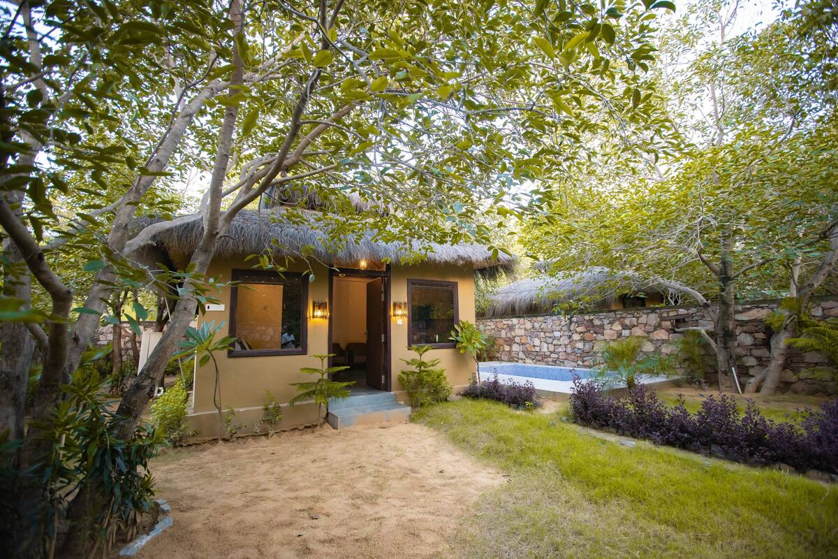 A thatched-roof building with a stone wall and a small pool.