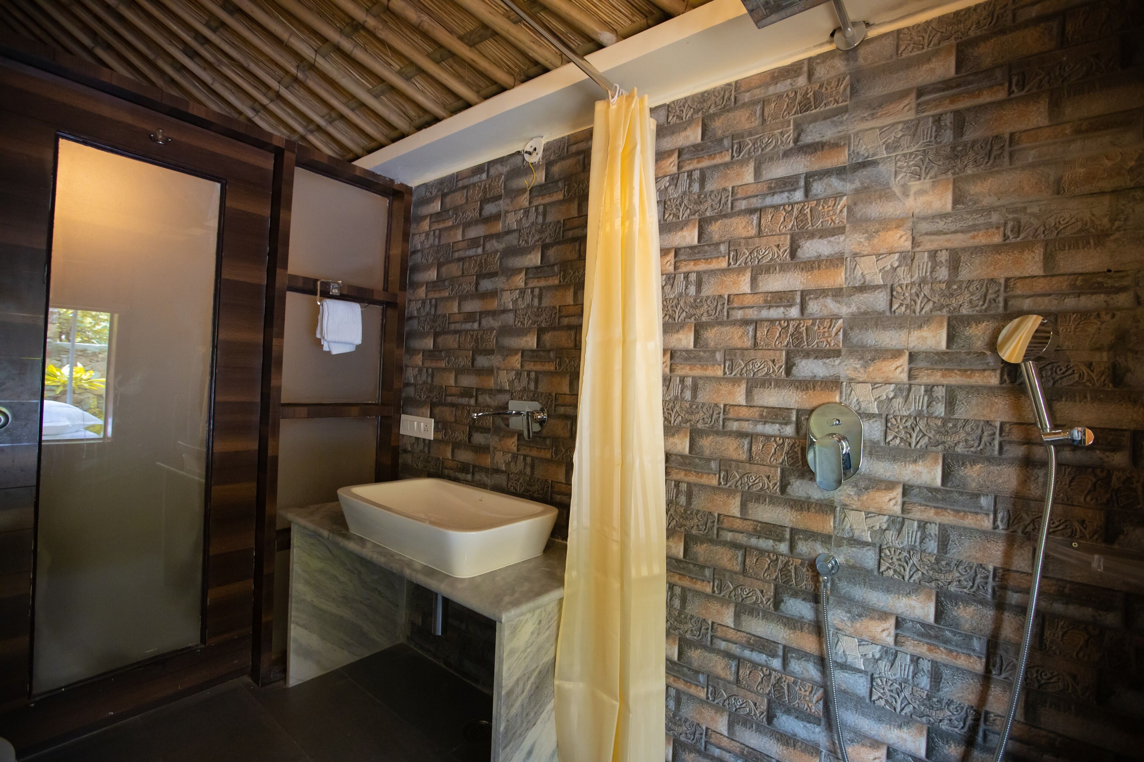 A bathroom with a stone wall, a sink, a shower, and a wooden ceiling.
