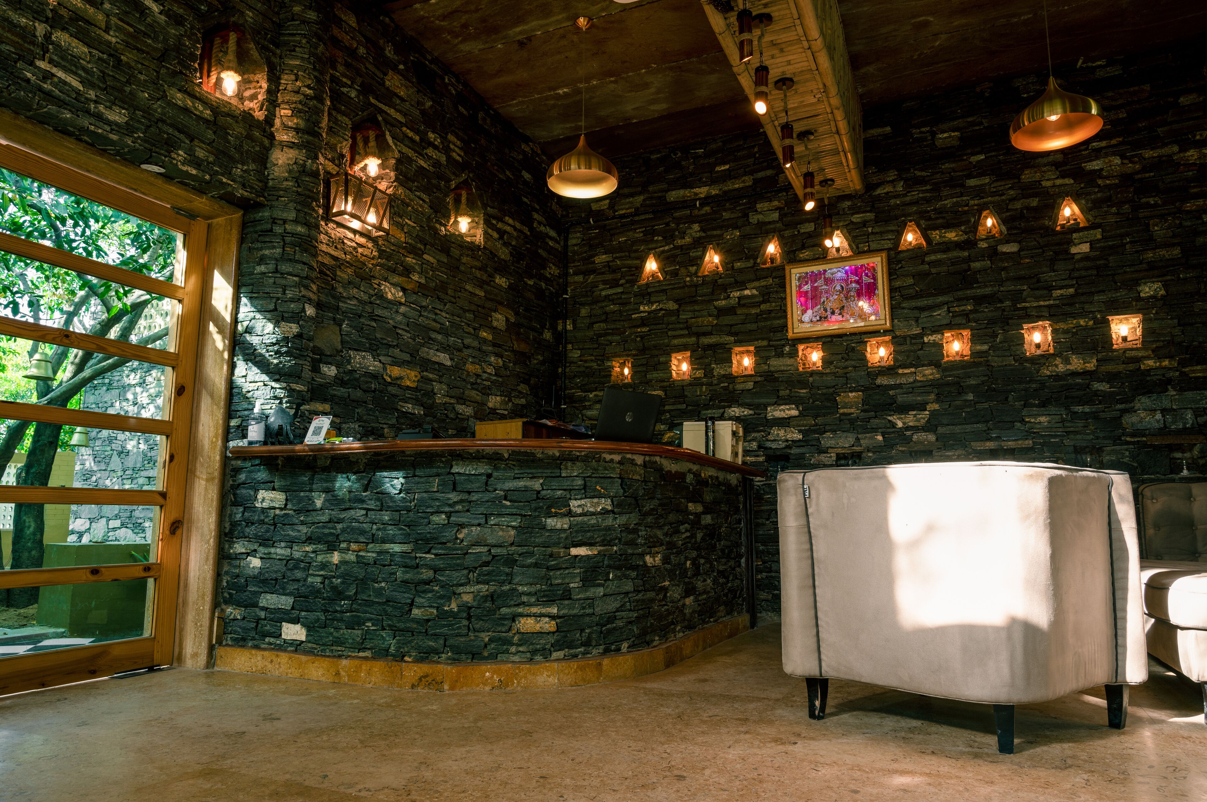Zona de recepción con paredes de piedra, un mostrador de madera, iluminación colgante y un sillón blanco.