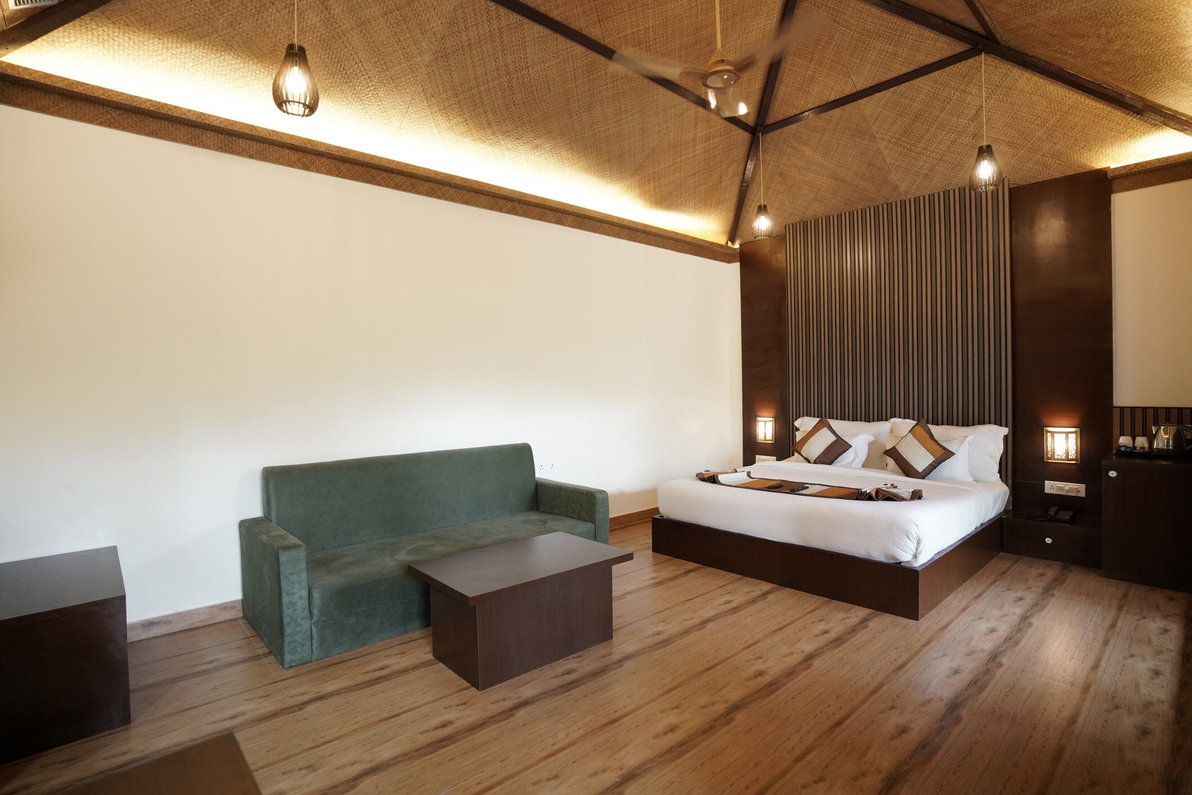 Una habitación de hotel con una cama, un sofá verde, una mesita de centro de madera y un ventilador de techo.