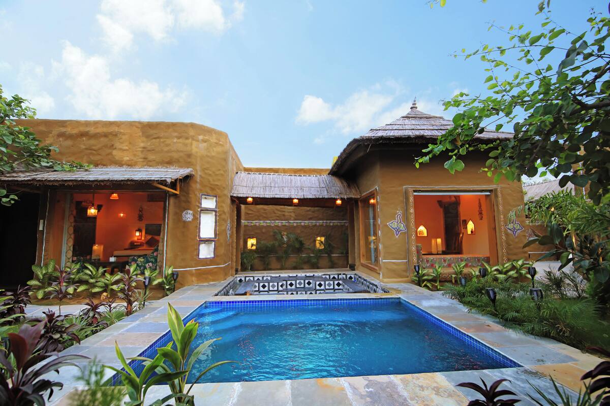 A pool area with a hot tub, surrounded by plants and a building with a thatched roof.