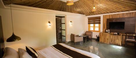 A modern hotel room with a large bed, a TV, a dining area, and a bamboo ceiling.