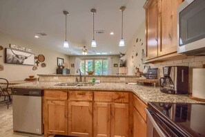 A kitchen with wooden cabinets, granite countertops, a dishwasher, a stove, and pendant lighting.