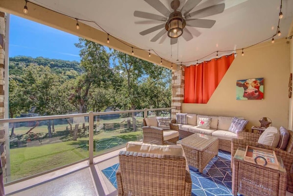 A balcony with wicker furniture, a ceiling fan, and a view of a green landscape. - RG 211 Guadalupe River Oasis (New Braunfels)