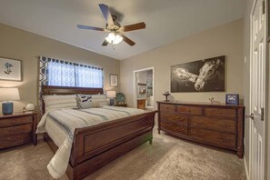A bedroom with a bed, dresser, ceiling fan, and artwork. - RG 211 Guadalupe River Oasis (New Braunfels)