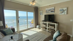 A living room with a large window, a ceiling fan, a television, and a sofa.