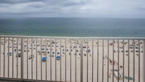 A beach with numerous umbrellas and people, viewed from a balcony.