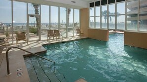 An indoor swimming pool with clear views of the sea through large windows, surrounded by lounge chairs.