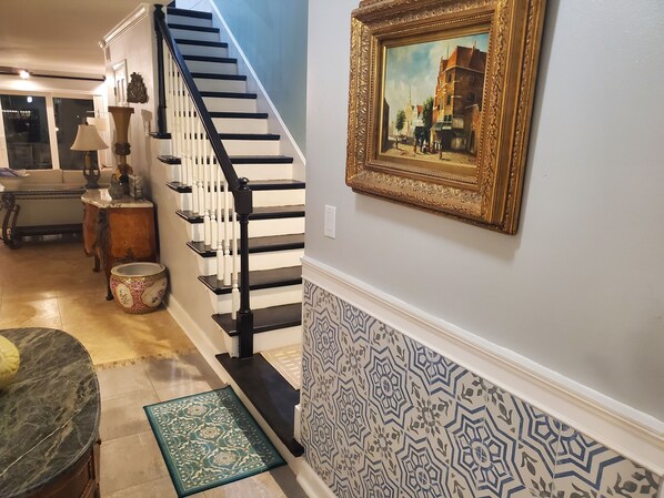 A staircase with black balusters, a patterned wall, a framed painting, and a marble countertop.