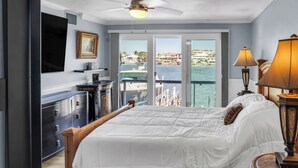 Un dormitorio con una cama grande, un televisor montado en la pared, un aparador y vistas al agua y edificios.