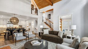 A spacious living area with a high ceiling, a dining area, and a staircase leading to another level.