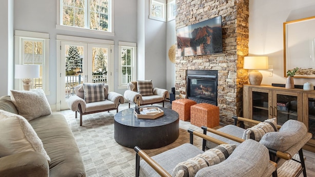 A spacious living room with a stone fireplace, comfortable seating, and large windows.