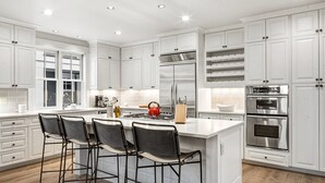 A modern kitchen with white cabinetry, stainless steel appliances, and a central island with bar stools.