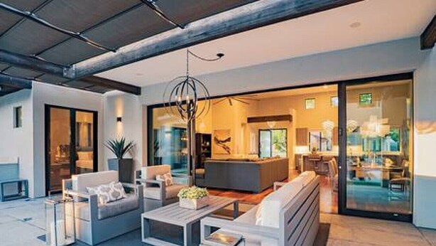 A modern interior with a seating area featuring sofas and a coffee table, a kitchen visible through glass doors, and a hanging light fixture. - Arcadia Luxury 4 Bedroom 4EnSuite Bath Heated Pool (Phoenix)