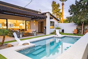 Een modern huis met een zwembad, buitenmeubilair en een keurig onderhouden tuin.