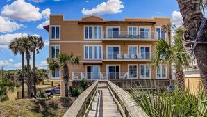 A multi-story hotel with a wooden deck leading to the entrance, surrounded by palm trees and a clear sky. - Sea View is at the Beach! (Fernandina Beach)