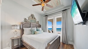 A bedroom with a wooden bed, a nightstand, a ceiling fan, and a large window with a view of the beach. - "Tide Life" - Perfect Sized Family Beach House (Panama City Beach)