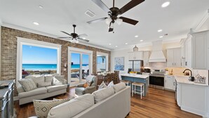 A spacious living area with a large sofa, a dining table, and a kitchen area with white cabinets and a view of the ocean. - "Tide Life" - Perfect Sized Family Beach House (Panama City Beach)