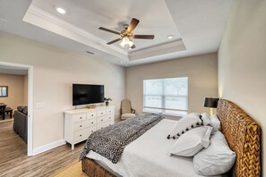 A bedroom with a bed, a TV, a ceiling fan, a window with blinds, and a nightstand.