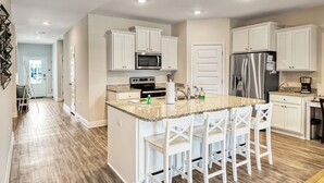 A modern kitchen with white cabinetry, a granite countertop, stainless steel appliances, and a central island with bar stools. - Port St. Joe Home | Heated Pool | Dog Friendly | Sleeps 10 (Port St Joe)