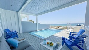 Un espacio al aire libre techado con piscina, sillas de descanso y una mesa con comida y bebidas.