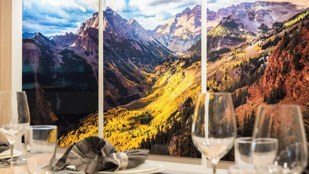 Ein Esstisch mit Blick auf die Berge durch ein Fenster, Gläser und einer Servietten.