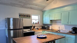 Eine Küche mit hellblauen Schränken, einem Edelstahlkühlschrank, einem Holztisch und einer weißen Spüle.