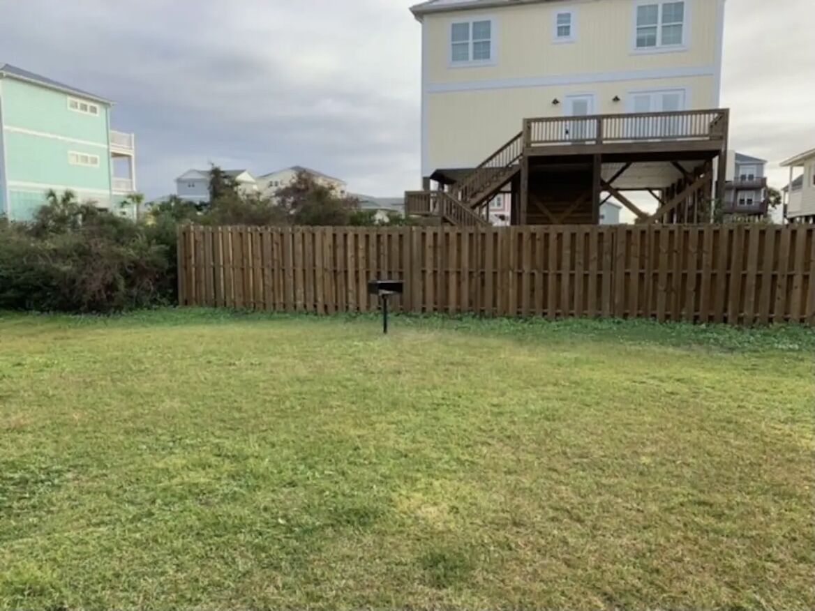 A fenced yard with a wooden deck and a building in the background.