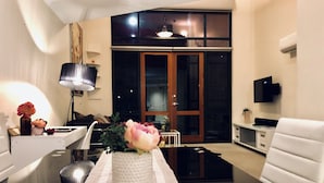 A modern living room with a white sofa, a dining table with a vase of flowers, a lamp, and a TV mounted on the wall. - Forum Central City Loft with Free Wi-Fi and Parking (Canberra)