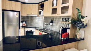 A modern kitchen with a black countertop, stainless steel appliances, wooden cabinets, and a small island with bar stools. - Forum Central City Loft with Free Wi-Fi and Parking (Canberra)