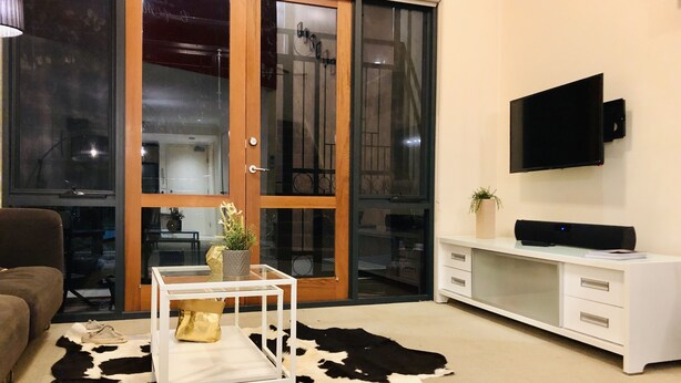 A living room with a glass door, a flat-screen TV, a white desk, and a cowhide rug. - Forum Central City Loft with Free Wi-Fi and Parking (Canberra)