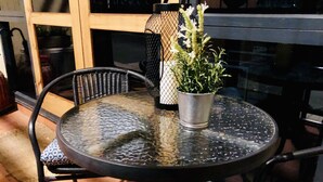 A round glass table with a metal frame, accompanied by two wicker chairs with patterned cushions. A potted plant is placed on the table. - Forum Central City Loft with Free Wi-Fi and Parking (Canberra)