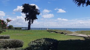 Een kustlandschap met een gazon, een pad en uitzicht op zee met boten.