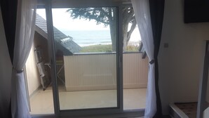 Een kamer met een schuifdeur die uitkomt op een balkon. Het balkon heeft een houten omheining en uitzicht op zee.