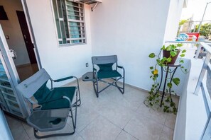A balcony with two green folding chairs, a potted plant, and a window with bars. - Loft Oasis (Playa del Carmen)