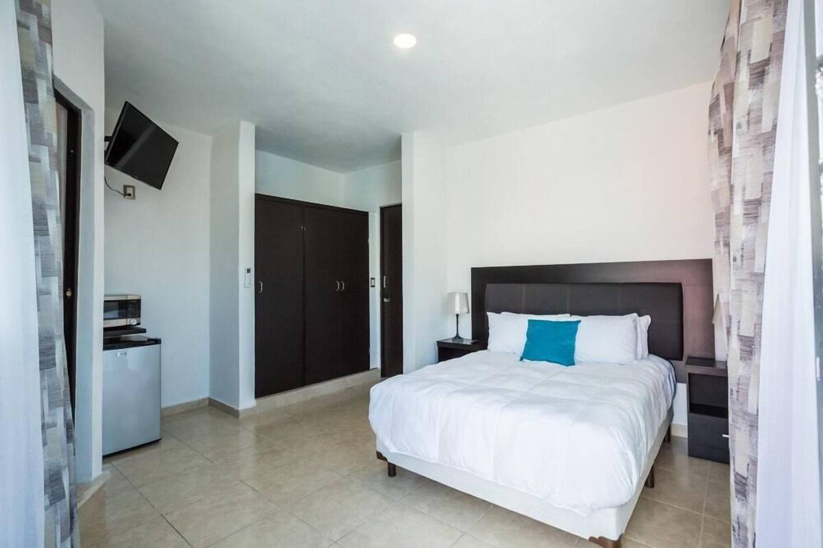 A bedroom with a bed, a TV mounted on the wall, a desk, and a wardrobe.