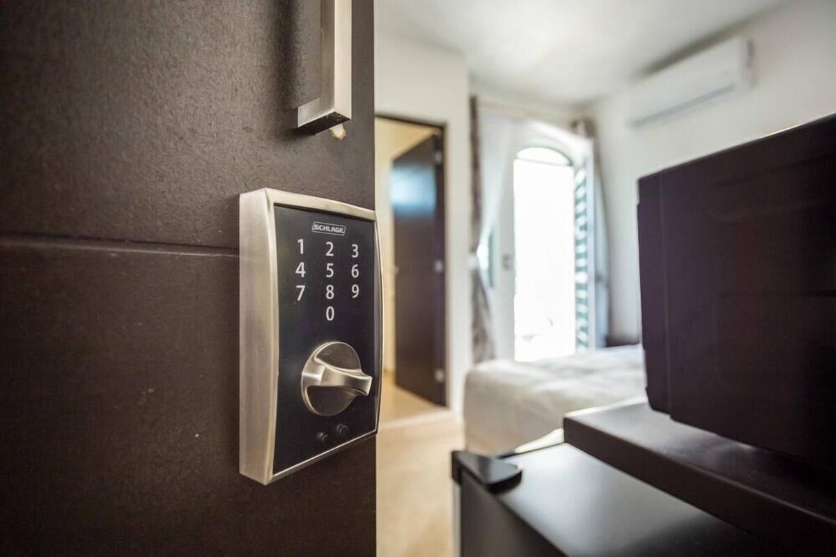 A modern room with a built-in electronic keypad door lock, a bed, and a window with curtains.